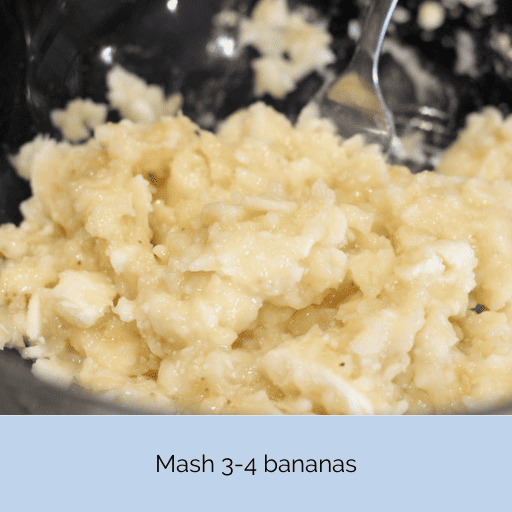 Mashed bananas in a glass bowl with a stainless steel fork.