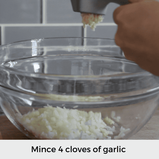 mincing garlic into a glass bowl with chopped onion in the bowl
