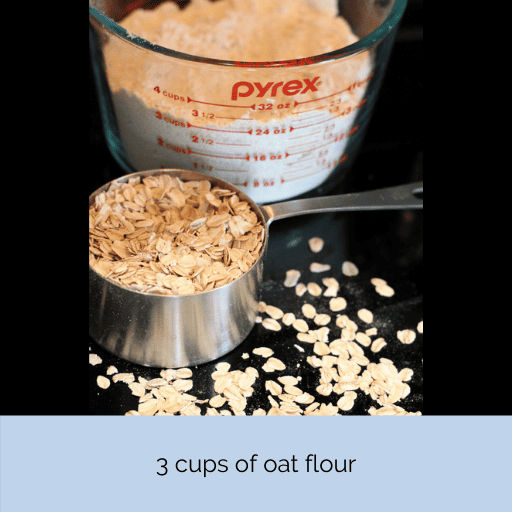 A large glass measuring cup filled with oat flour sitting on a black stovetop. In front of it is a stainless steel 1 cup measuring cup filled with rolled oats. Rolled oats are also scattered on the stovetop.