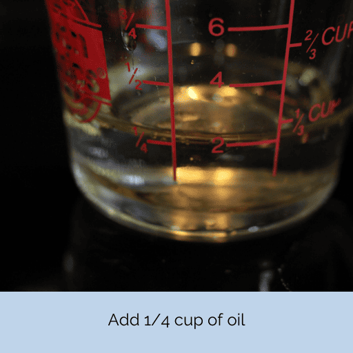 1/4 cup of olive oil in a glass measuring cup sitting on a black surface with a black background.