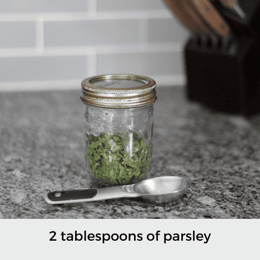 a tablespoon sitting in front of a pint jar of dried parsley