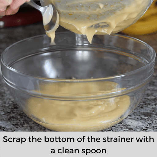 scraping the bottom of the strainer with a clean spoon over the glass bowl.