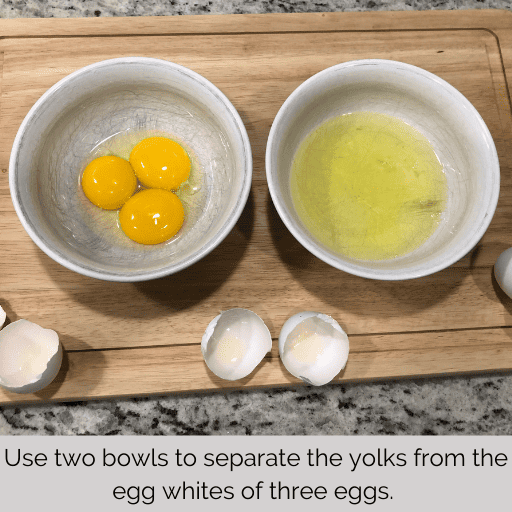 two white bowls sitting on a cutting board. The one on the left has three egg yolks and the one on the right has three egg whites.