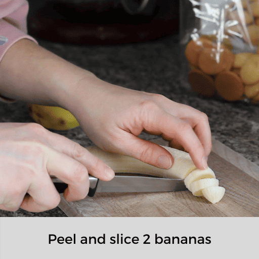 slicing a peeled banana on a wooden cutting board.