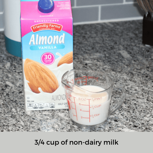 three fourths cup of almond milk in a glass measuring cup sitting in front of the carton on the counter 