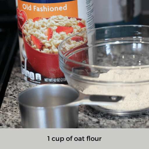 one cup measuring cup sitting on the counter in front of a glass bowl filled with oat flour. A container of old fashioned oats is sitting behind the bowl.