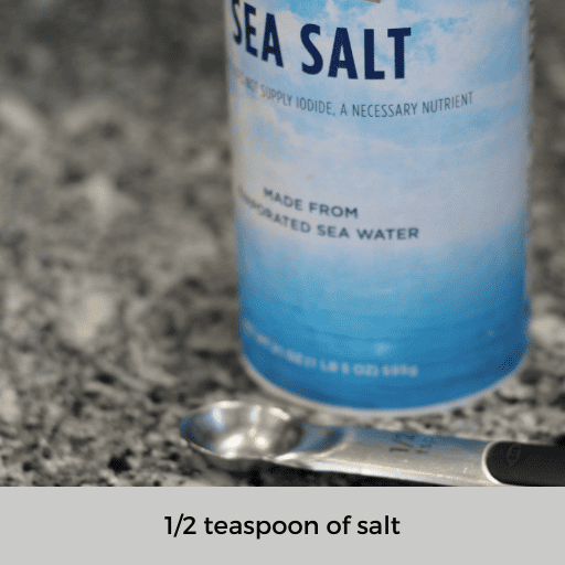 container of sea salt sitting behind a half teaspoon measuring spoon