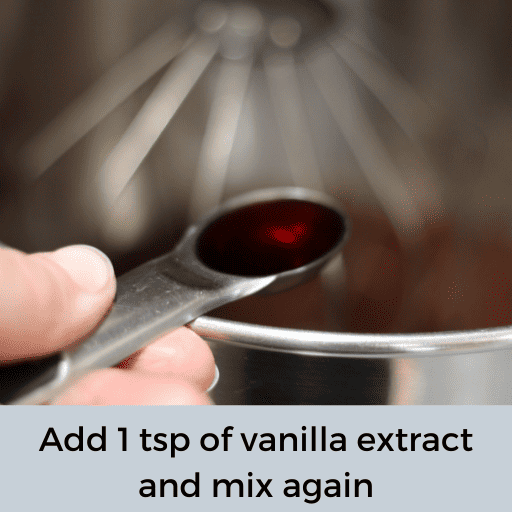 hand holding a tsp of vanilla above a stainless steel mixing bowl