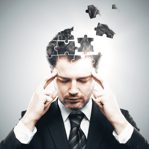 businessman holding fingertips to his temples. His head is breaking apart into puzzle pieces. 
