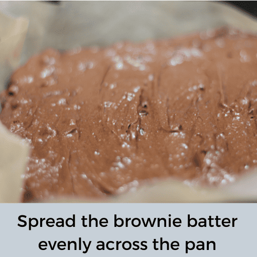 gluten and dairy free brownie batter spread out in a baking dish lined with parchment paper