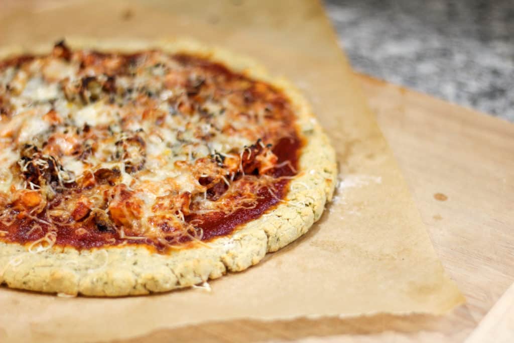 Gluten and dairy free pizza on parchment paper sitting on a cutting board on the counter. 