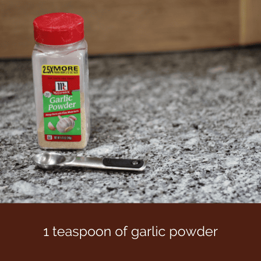 container of garlic powder with a teaspoon sitting in front of it. 