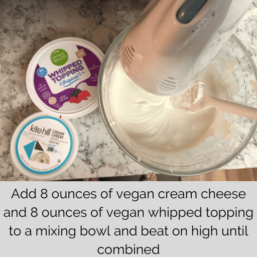 white mixer with a glass mixing bowl mixing up a container of vegan cream cheese and whipped topping