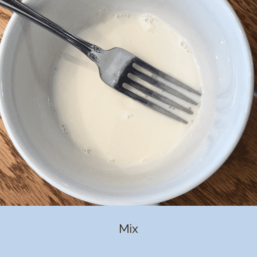 fork sitting in a small white cup with a little bit of creamy white mixture in it