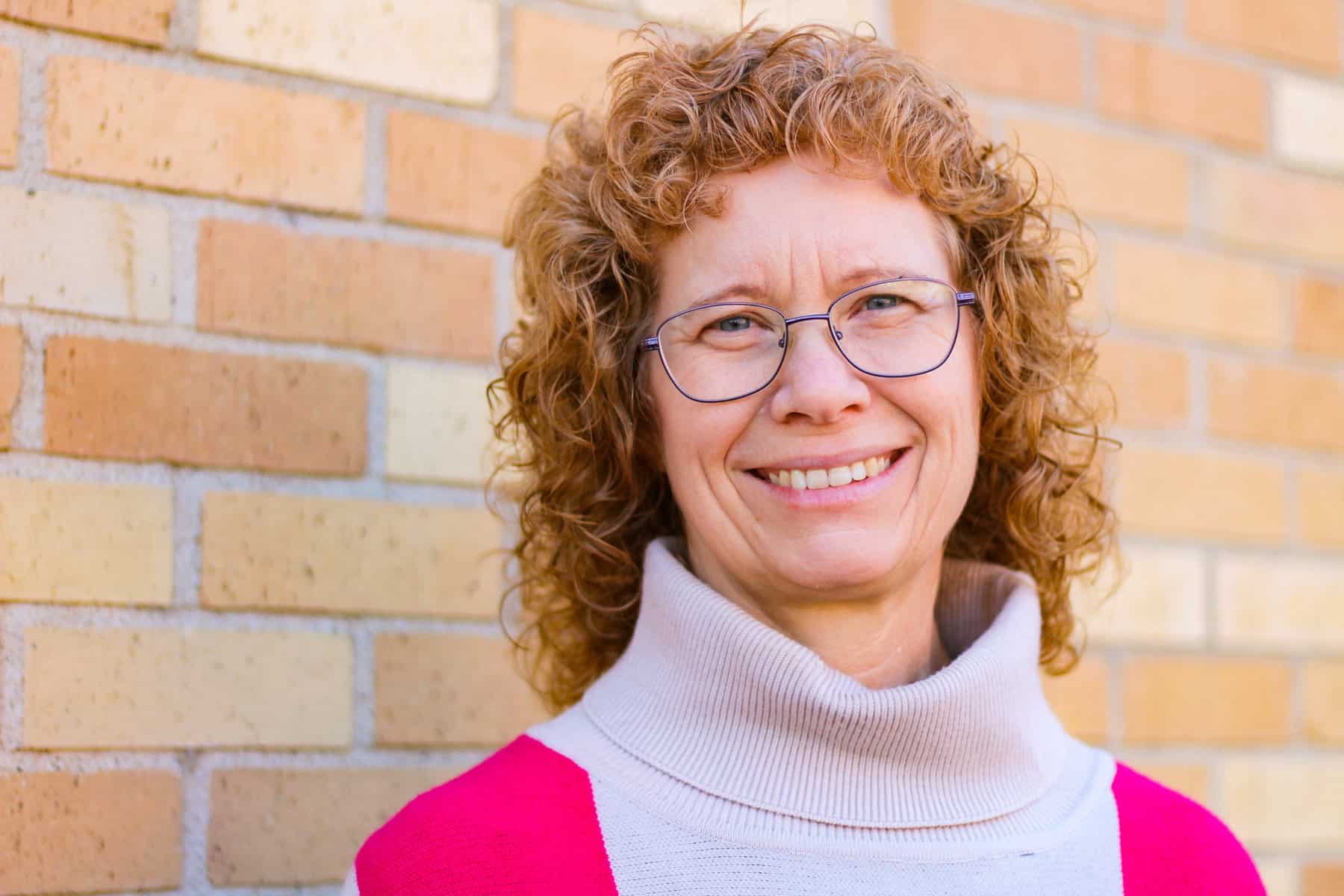 Cheri Moore smiling standing against a tan brick wall