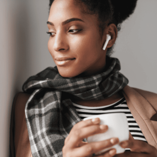 African American woman with hearing difficulties wearing white earbuds sipping on a cup of coffee leaning up against a wall