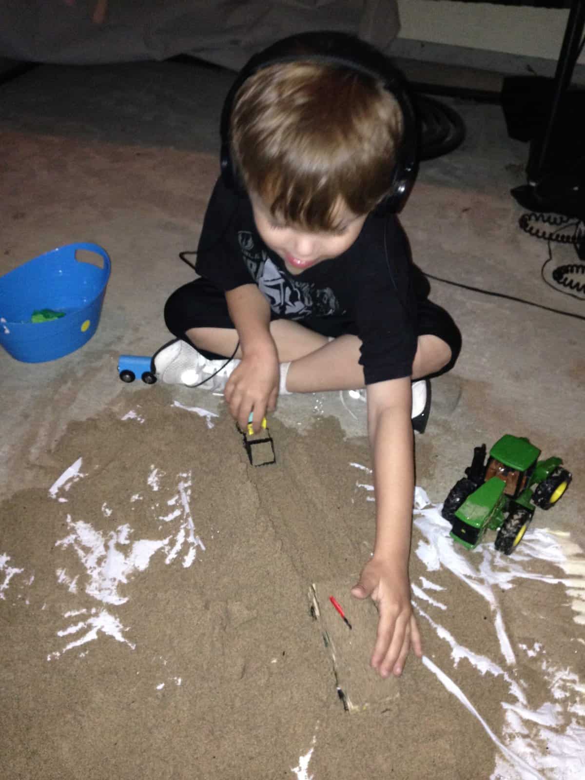 Preschooler wearing headphones listening to In-home Berard-Based Auditory Integration Training playing in the sand with trucks