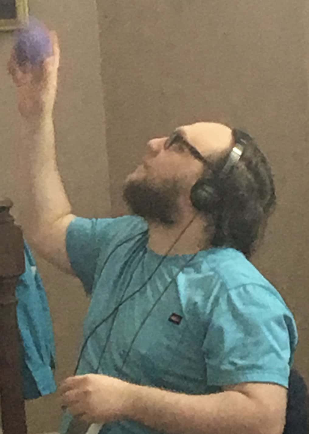 Young man wearing headphones listening to therapeutic music while tossing a stress ball up into the air.