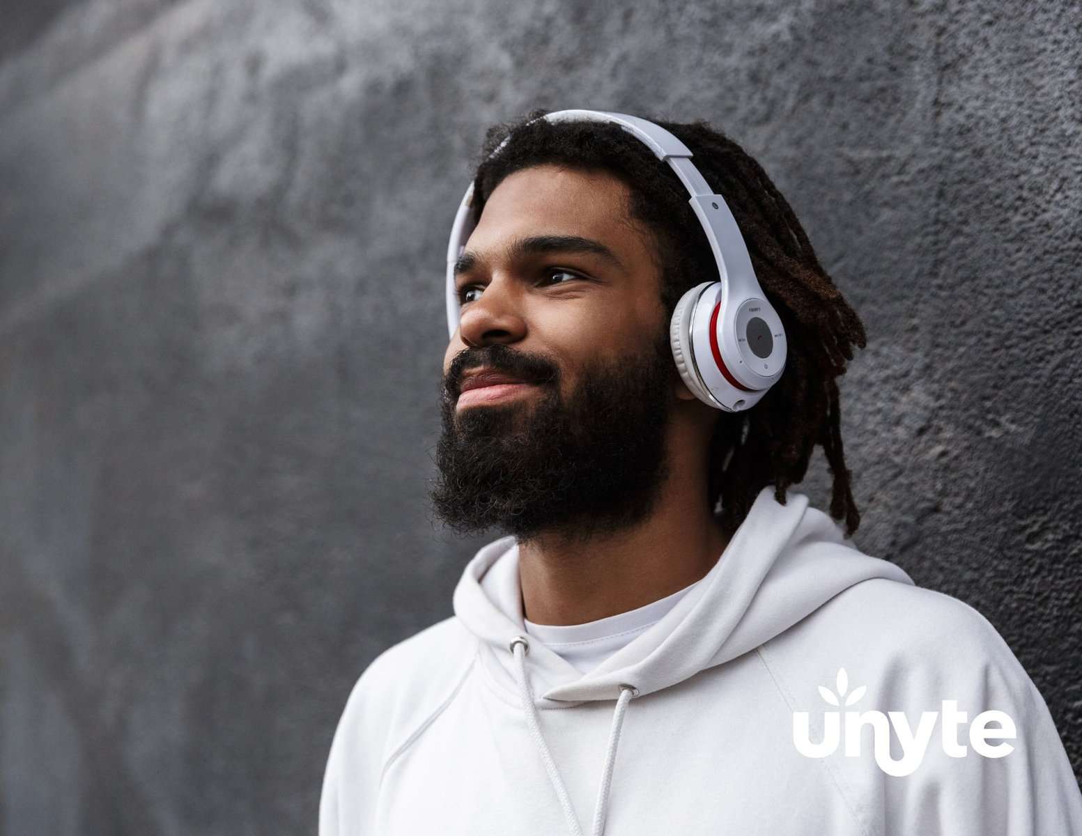 African American male with a black beard and mustache wearing white headphones and a white hooded sweatshirt. 